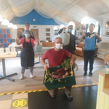 Five people at Swallow cafe wearing masks, receiving donated bags and a box vegetables.