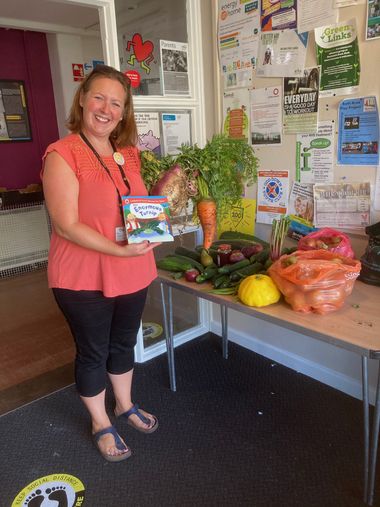 A person at Bath Area Play Project posing with donated vegetables on a table